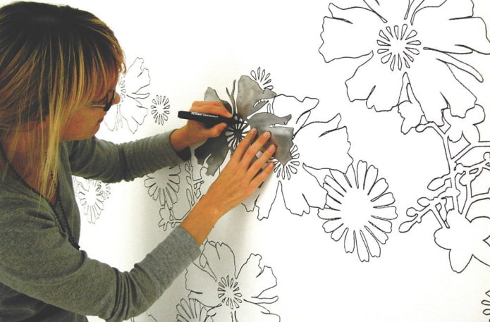 vrouw schildert bloemen op de muur met behulp van een stencil